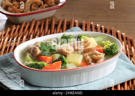 Hähnchenfüße, klare Suppe, leichte Brühe mit Brokkoli, Karotten und Kartoffel auf Keramikschüssel. Beliebt als SOP Ceker in Indonesien Stockfoto