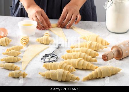 In der Bäckerei werden klassische Croissants hergestellt. Frau rollt den Teig zu Brötchen für das weitere Backen. Französische Backwaren. Stockfoto