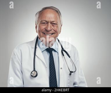 Auf dem Weg durch das Krankenhaus. Aufnahme eines glücklichen älteren männlichen Arztes im Studio vor grauem Hintergrund. Stockfoto