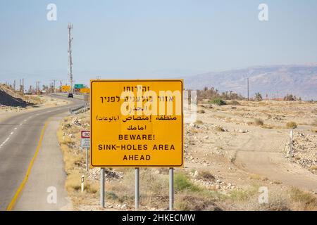 Ein dreisprachiges Warnschild entlang des israelischen Highway 90 warnt vor Sinklöchern in diesem Gebiet der Judäischen Wüste nahe dem Toten Meer im Westjordanland. Stockfoto