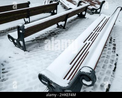 Bänke in einem Park, der an frostigen, verschneiten Tagen mit frischem Erstschnee bedeckt ist Stockfoto