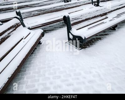 Schnee auf Bänken und Wanderwegen im Park. Kalter Wintertag. Stockfoto