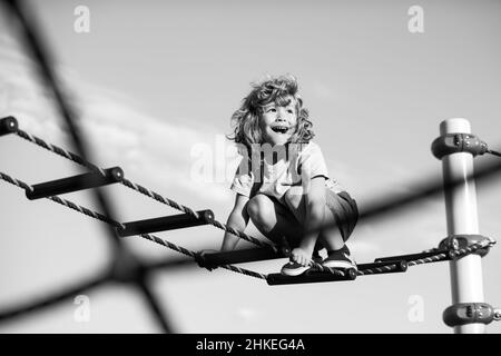 Netter Junge klettert die Leiter auf dem Spielplatz hoch. Kind klettert die Leiter gegen den blauen Himmel hinauf. Platz für Text kopieren. Stockfoto