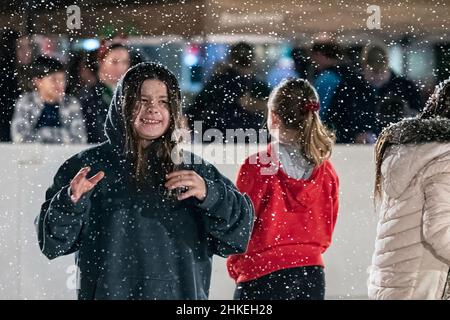 Prattville, Alabama, USA - 23. Dezember 2021: Ein Mädchen lächelt und lacht, als künstlicher Schnee auf sie auf der Eislaufbahn im historischen Downtow fällt Stockfoto