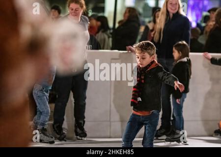 Prattville, Alabama, USA - 23. Dezember 2021: Der kleine Junge mit einem Schal macht sich vorsichtig auf den Weg über die Eislaufbahn im historischen Stadtzentrum von Prattvil Stockfoto