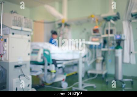 Schwer erkrankte Patientin, die auf der Intensivstation von medizinischen Technologien umgeben ist. Die Ärztin steht am Patientenbett und arbeitet mit Geräten. Unfokussierter Hintergrund Stockfoto