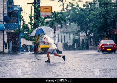 Kind, das während eines starken Regensturms im Zentrum von Manila, Philippinen, mit Regenschirm über die Straße läuft Stockfoto