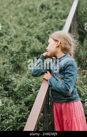 Nachdenklich ehrliche acht Jahre alte Mädchen steht auf Treppe mit Gras und genießen die Natur. Vorpubertal Alter der Kinder und ihr Leben, Geist psycho Stockfoto