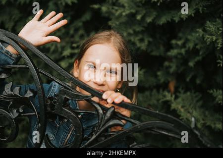 Portrait nachdenklich seriöse ehrliche acht Jahre alte Mädchen Gesicht späht aus abstrakten Metallformen in der Natur. Vorpubertär Alter der Kinder und ihre Stockfoto