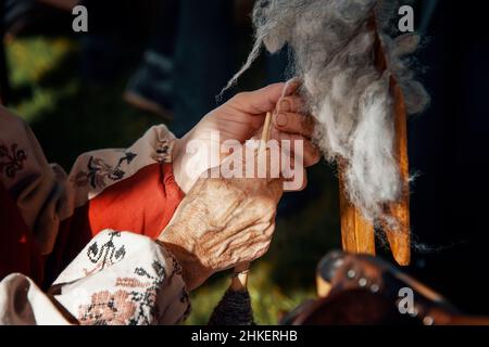 Hände einer alten Frau. Hände spinnen Garn auf einem alten Spinnrad. Ein altes Frauenhandwerk. Stockfoto