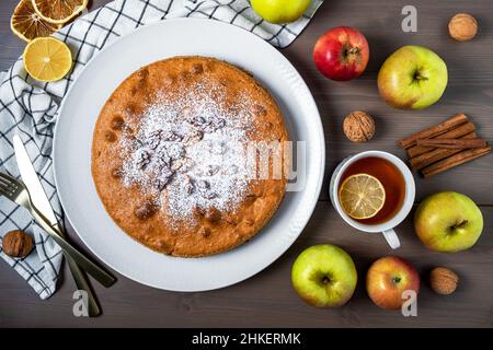 Nahaufnahme eines Apfelkuchens von oben, umgeben von frischen reifen Äpfeln. Hausgemachte Kuchen mit saisonalen Früchten, DIY. Selektiver Fokus. Stockfoto