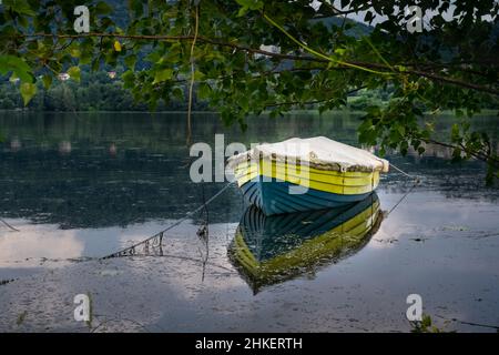 Das kleine Boot, eingerahmt von grünen Zweigen, spiegelt sich im Wasser des Sees wider. Revine Lago, Treviso, Italien Stockfoto