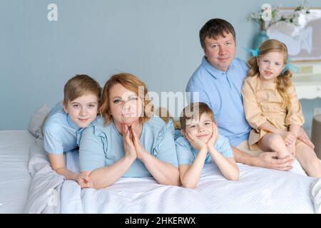 Glückliche Familie, die auf ihrem Bett im Schlafzimmer die Kamera ansah. Kaukasische Eltern und Kinder liegen und haben Spaß zu Hause in ihrer Freizeit. Große freundliche Familie ruht sich im Urlaub aus. Söhne und süße Tochter Stockfoto