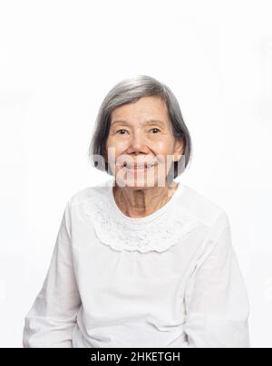 Porträt einer niedlichen lächelnden älteren asiatischen Frau, die isoliert auf Weiß auf die Kamera schaut. Ältere alte Dame Nahaufnahme Porträt. Stockfoto