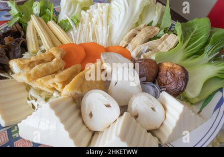 Mehrere frische Gemüse, Tofu und Pilze werden auf einen Teller gelegt. Stockfoto