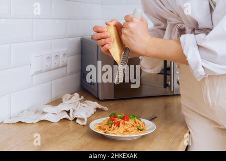 Nahaufnahme der weiblichen Hände reiben Parmesan auf einer Reibe Stockfoto