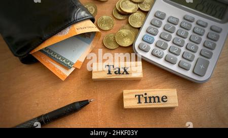 Tax Time Text auf Holzblöcken mit Taschenrechner-Stift und Geld Hintergrund. Steuerkonzept. Stockfoto