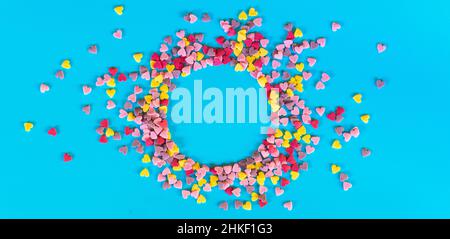 Flatlay-Mockup aus bunten Zuckerherzen auf türkisfarbenem Hintergrund in Form eines runden Rahmens Stockfoto