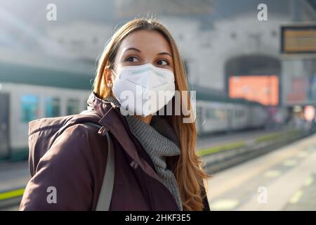 Porträt einer lässigen Frau, die im Winter mit KN95 FFP2 Schutzmaske am Bahnhof wartet Stockfoto