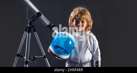 Das kleine Kind will mit einem Astronautenhelm und einem Teleskop im Weltraum fliegen. Speicherplatz kopieren. Astronomie und Astrologie Konzept. Stockfoto