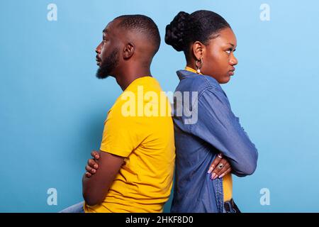 Zornige Partner, die sich im Studio mit gekreuzten Armen Rücken an Rücken lehnen. Vereister Freund und Freundin mit Beziehungsproblemen und Streit vor der Kamera. Entferntes verärgertes Paar Stockfoto