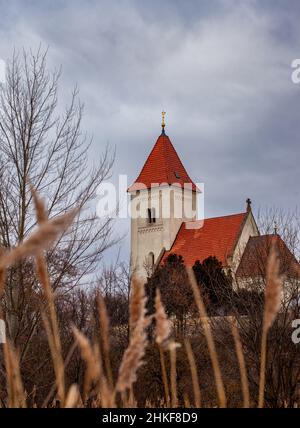 Eine Kirche steht vor einem dunklen Himmel. Unscharfes trockenes Schilf ist im Vordergrund. Stockfoto