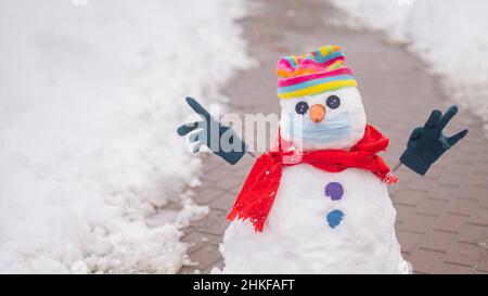 Schneemann in einem Regenbogenhut und einer medizinischen Maske. Stockfoto