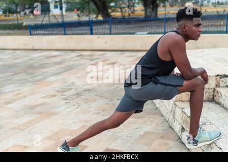 Afroamerikanischer Mann in Sportkleidung, der sich auf der Straße streckt Stockfoto