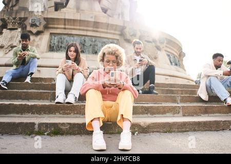 Gruppe von individualistischen Menschen, die im Freien telefonieren und ernsthaftes Gesicht haben. Freunde konzentrierten sich auf ihre Handys, die sich gegenseitig im Freien ignorierten. Technologie Stockfoto