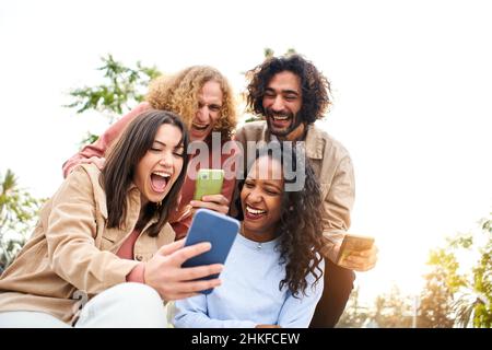 Glückliche Freunde, die mit einem überraschten Gesicht und einem Lächeln das Handy auf dem Bildschirm sehen. Junge Erwachsene mit Smartphone und Spaß. Stockfoto