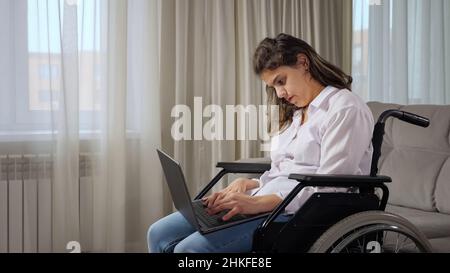 Eine behinderte Frau arbeitet online auf einem Laptop, der im Rollstuhl sitzt Stockfoto