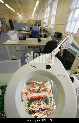 Techniker im Labor, der eine große beleuchtete Lupe verwendet, um elektrische Bauteile und Leiterplatten anzuzeigen. Stockfoto
