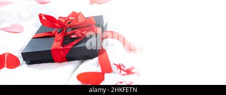 Geschenkbox verpackt und Postkarte mit einer roten schönen Schleife auf dem Bett dekoriert. Valentinstag, Geburtstagsgeschenk. Konzept für Hochzeitsreisende. Liebhaber Stockfoto