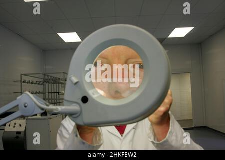 Techniker im Labor, der eine große beleuchtete Lupe verwendet, um elektrische Bauteile und Leiterplatten anzuzeigen. Stockfoto