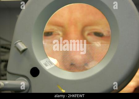Techniker im Labor, der eine große beleuchtete Lupe verwendet, um elektrische Bauteile und Leiterplatten anzuzeigen. Stockfoto