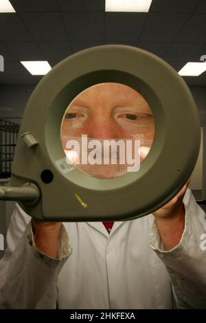Techniker im Labor, der eine große beleuchtete Lupe verwendet, um elektrische Bauteile und Leiterplatten anzuzeigen. Stockfoto