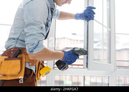 Mann, der das Schloss mit einem elektrischen Schraubendreher am Fenster festgemacht hat Stockfoto