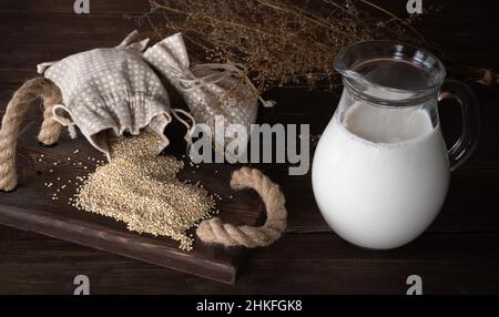 Verstreute Quinoa-Körner und ein Krug Milch auf einem Holztisch. Chenopodium Quinoa. Milch aus Quinoa. Stockfoto