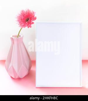 Kunstvase mit einer rosa Gerbera-Blume und weißem leeren vertikalen Rahmen auf zweifarbigem rosa-weißem Hintergrund. Kreative Minimalmockup. Valentinstag, Moth Stockfoto