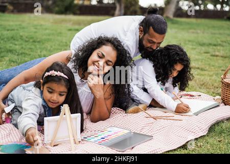 Glückliche indische Familie mit Spaß malen mit Kindern im Freien im Stadtpark - Fokus auf Mutter Gesicht Stockfoto