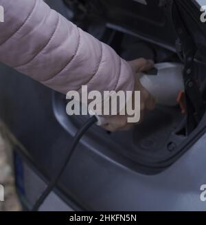 Frau lädt Elektroauto an der Ladestation. Spannungs- und Stromversorgungskonzept. Boxenstopp an der Ladestation. Öffentliche EV-Ladestation. Stockfoto