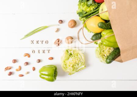 Gesundes veganes Essen in einer Papiertüte auf weißem Holzhintergrund. Gemüse, Obst, Nüsse. Das Konzept der Lebensmittelzustellung. Draufsicht Stockfoto