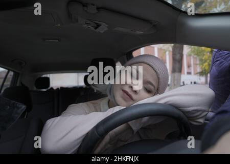 Müde asiatische Frau schlafen im Auto. Reife asiatische Frau schlief bei dem Auto auf einem Lenkrad ein. Blond mittleren Alters asiatische Frau im Auto. Frau auf der Straße. Geschäftskonzept. Stockfoto