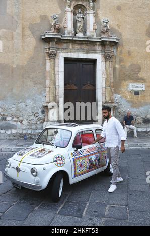 Italien, Sizilien, Taormina, junger Mann vor einem bunten Fiat 500 vor der Steinfassade der Kirche der Heiligen Katharina von Alexandria auf dem corso Umberto im mittelalterlichen Stadtzentrum Stockfoto
