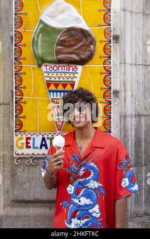 Italien, Sizilien, Taormina, junger Mann in buntem Hemd und Sonnenbrille mit Eis vor dem Gelatomania-Gletscher Stockfoto