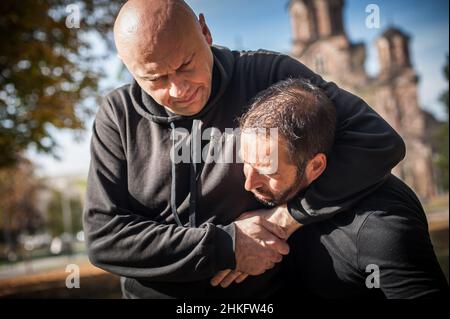 Zwei Männer streiten und kämpfen. Zwei Schläger kämpfen. Körperliche Konfrontation von Menschen draußen auf der Straße Stockfoto