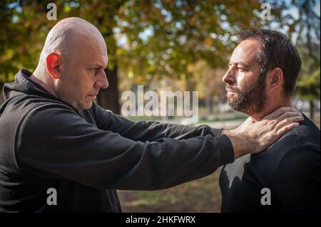 Zwei Männer streiten und kämpfen. Zwei Schläger kämpfen. Körperliche Konfrontation von Menschen draußen auf der Straße Stockfoto