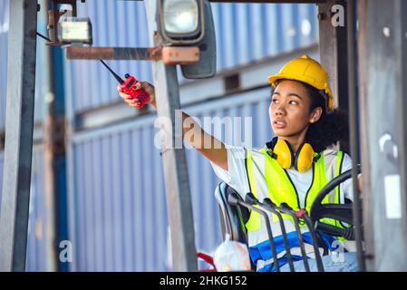 Weibliche Vorarbeiter verwenden Funkkommunikation, um während der Fahrt Gabelstapler auf Versand Containerhof zu kommunizieren. Shipping in Docks. Stockfoto