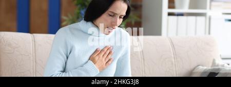 Junge Frau, die auf der Couch sitzt und hustet Stockfoto