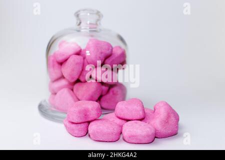 Nahaufnahme eines Glasglases mit rosa herzförmigen Bonbons auf weißem Hintergrund Stockfoto